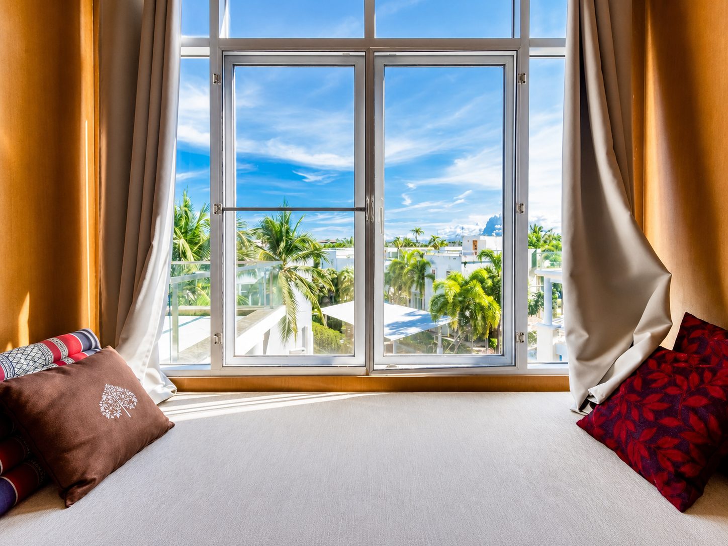 Bay-window day bed with floor-to-ceiling glass, palms and blue sky beyond